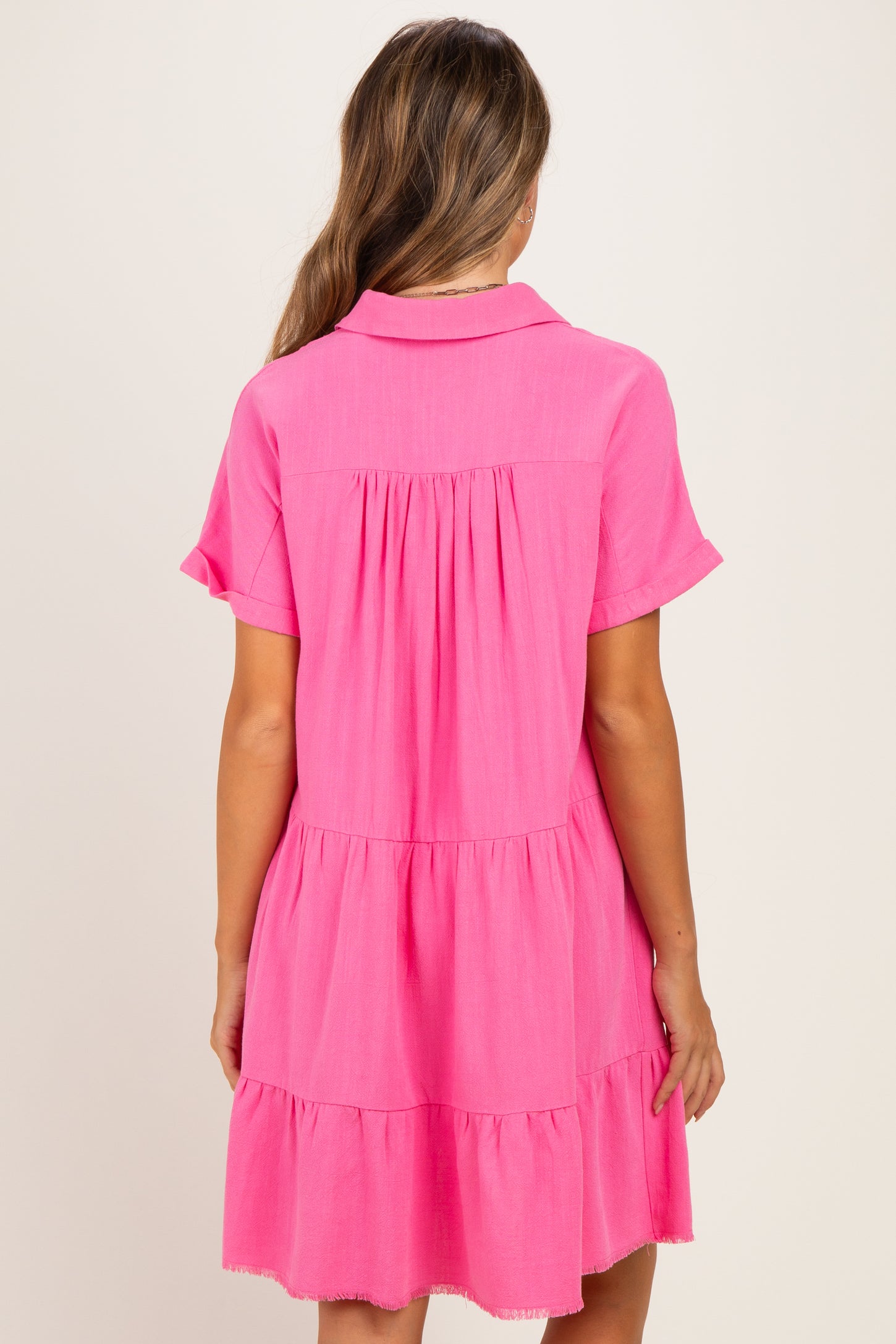 woman wearing a bright pink short sleeve maternity dress with tiered detailing and a collar, showing no visible baby bump