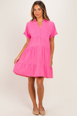 woman wearing a bright pink short sleeve maternity dress with a tiered design and a collar, holding her baby bump