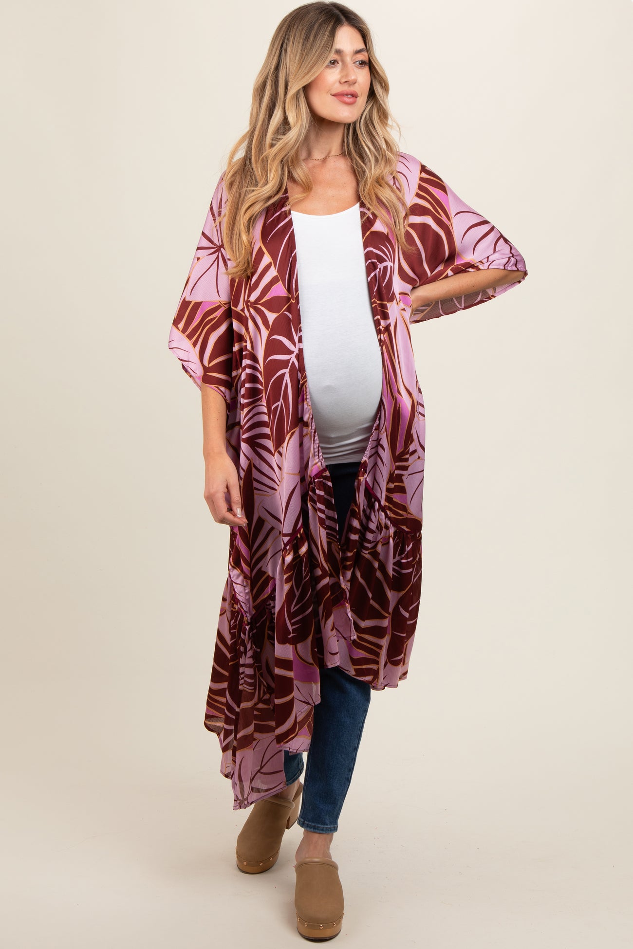woman wearing a colorful floral printed maternity kimono over a white tank top and jeans, showing her baby bump
