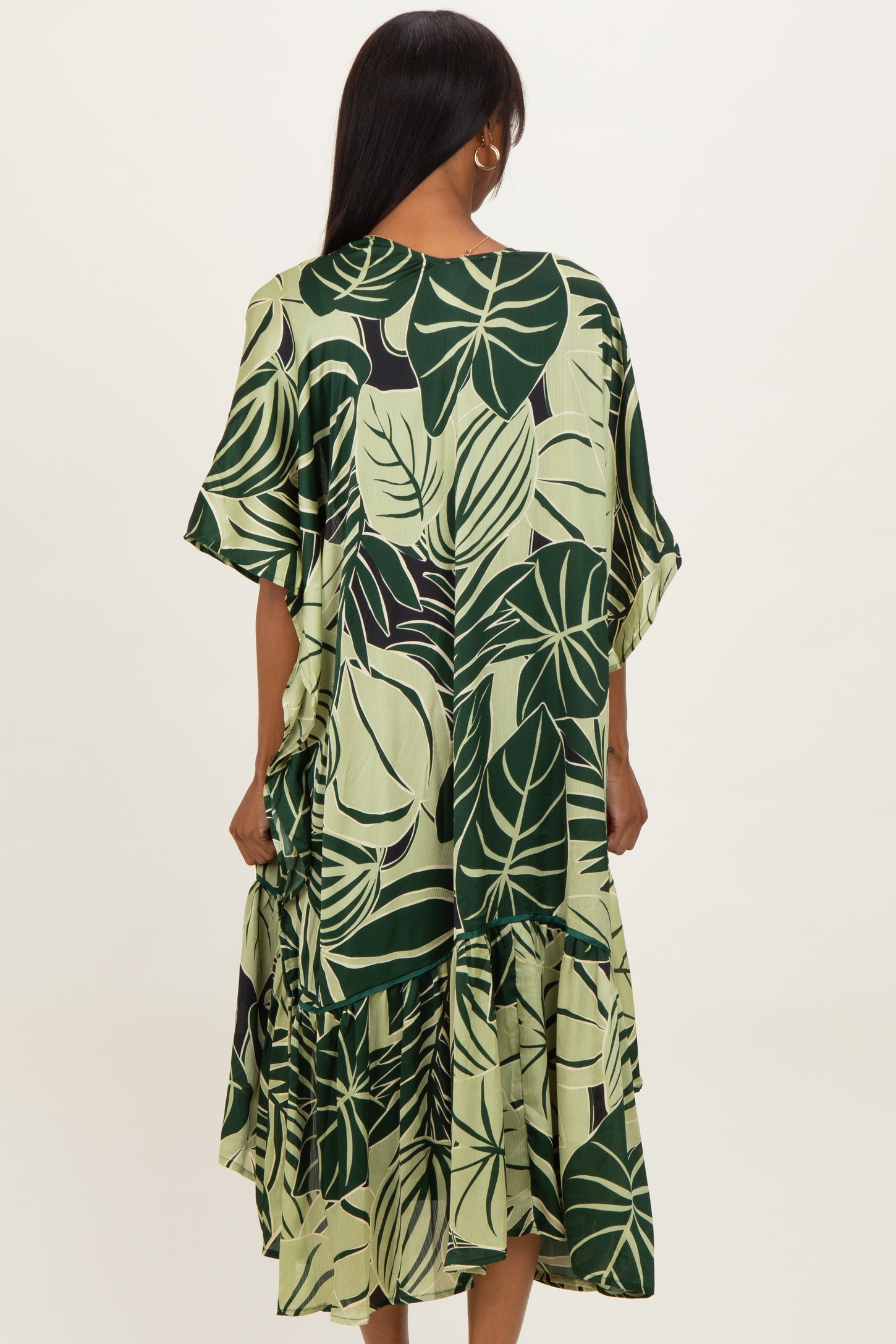 woman wearing a green tropical leaf print tiered dress with short sleeves from the back