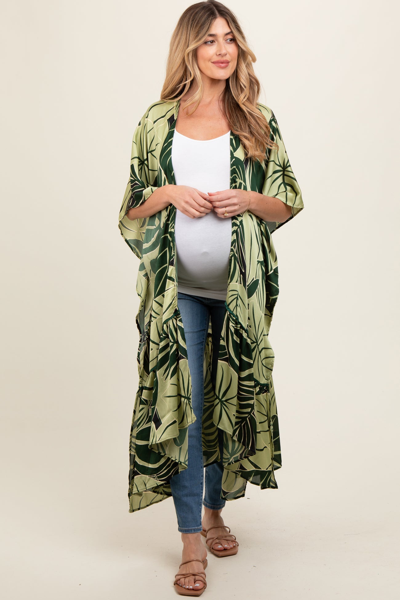 woman wearing a green palm leaf print maternity kimono over a white tank top and blue jeans, showcasing her baby bump