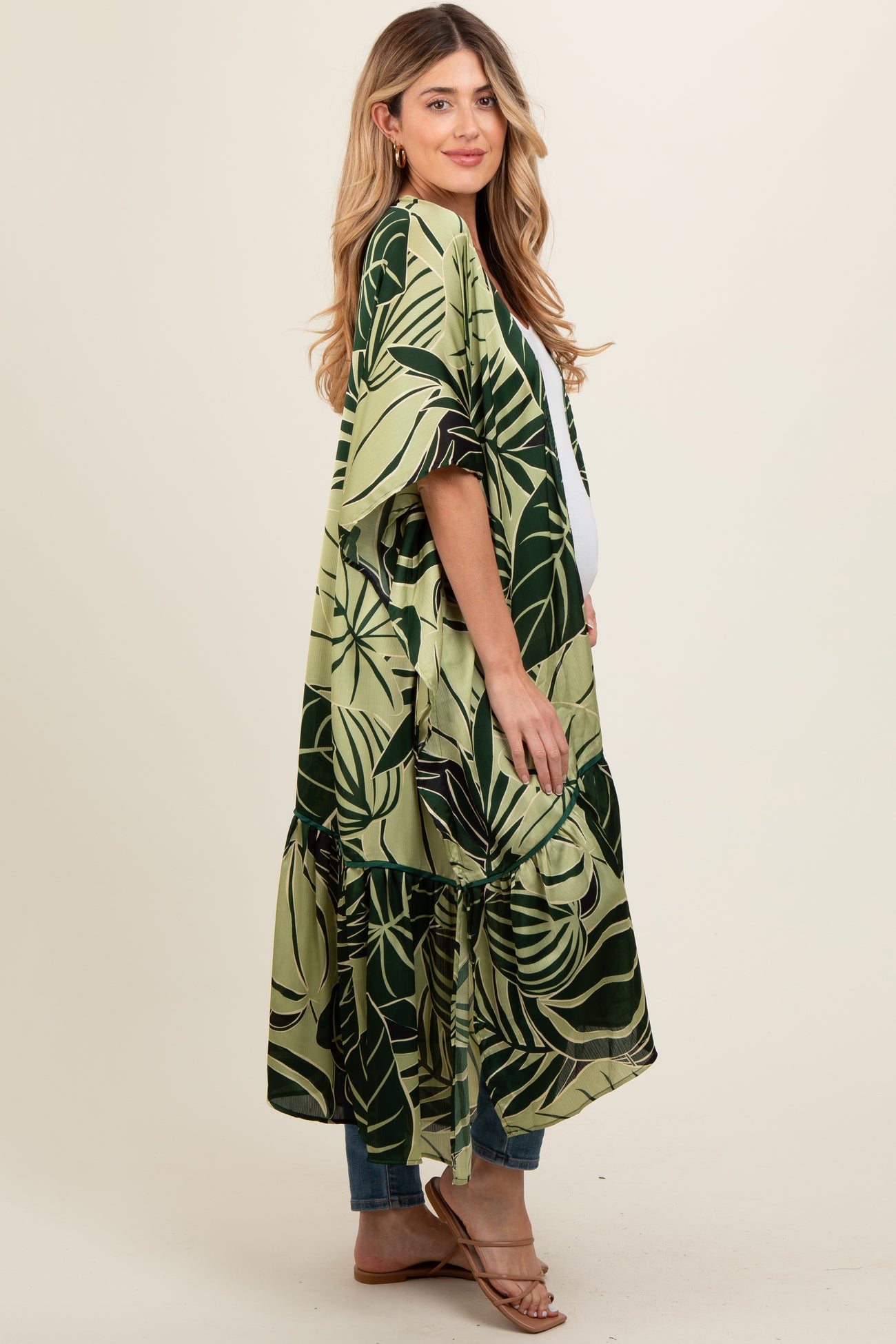 woman wearing a green and black leaf print maternity kimono over a white top and showing her baby bump