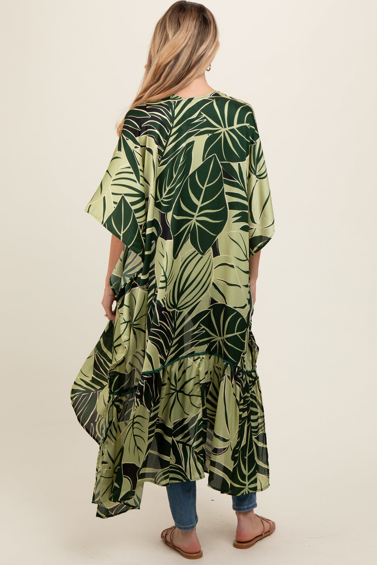 woman wearing a green leaf print maternity cover-up with a ruffled hem and open back, paired with jeans