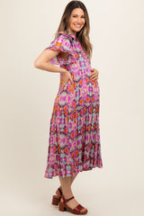 woman wearing a vibrant pink floral maternity dress with ruffled sleeves and holding her baby bump