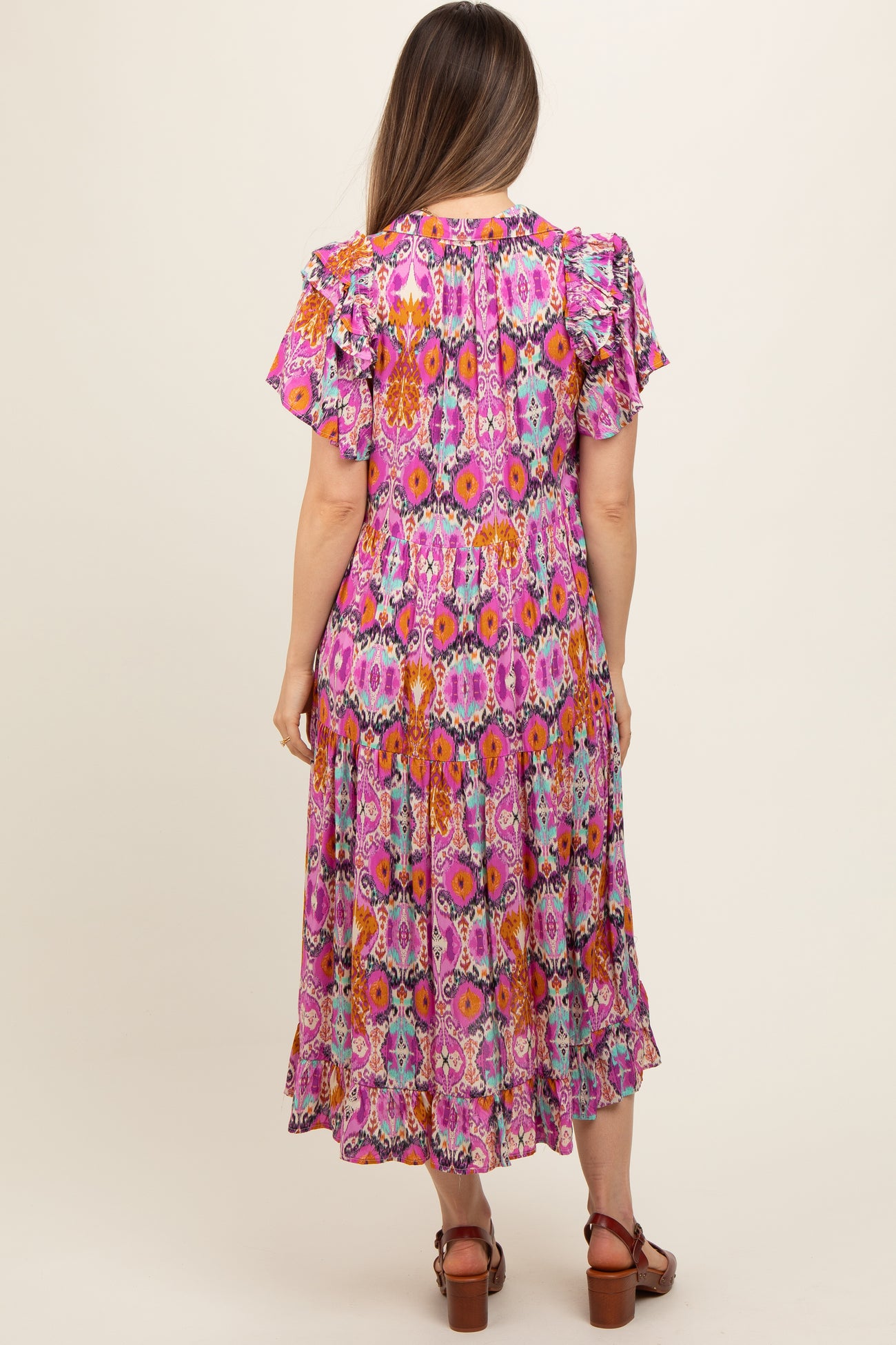 woman wearing a colorful floral print maternity dress with ruffle sleeves and a flowy skirt, showing her baby bump