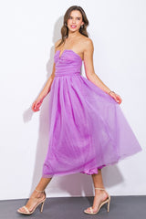 woman wearing a lilac strapless midi dress with a flowy skirt and ruching details, standing with one foot forward