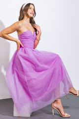 woman wearing a strapless lavender dress with a ruched bodice and a flowy tulle skirt, posing with one leg raised