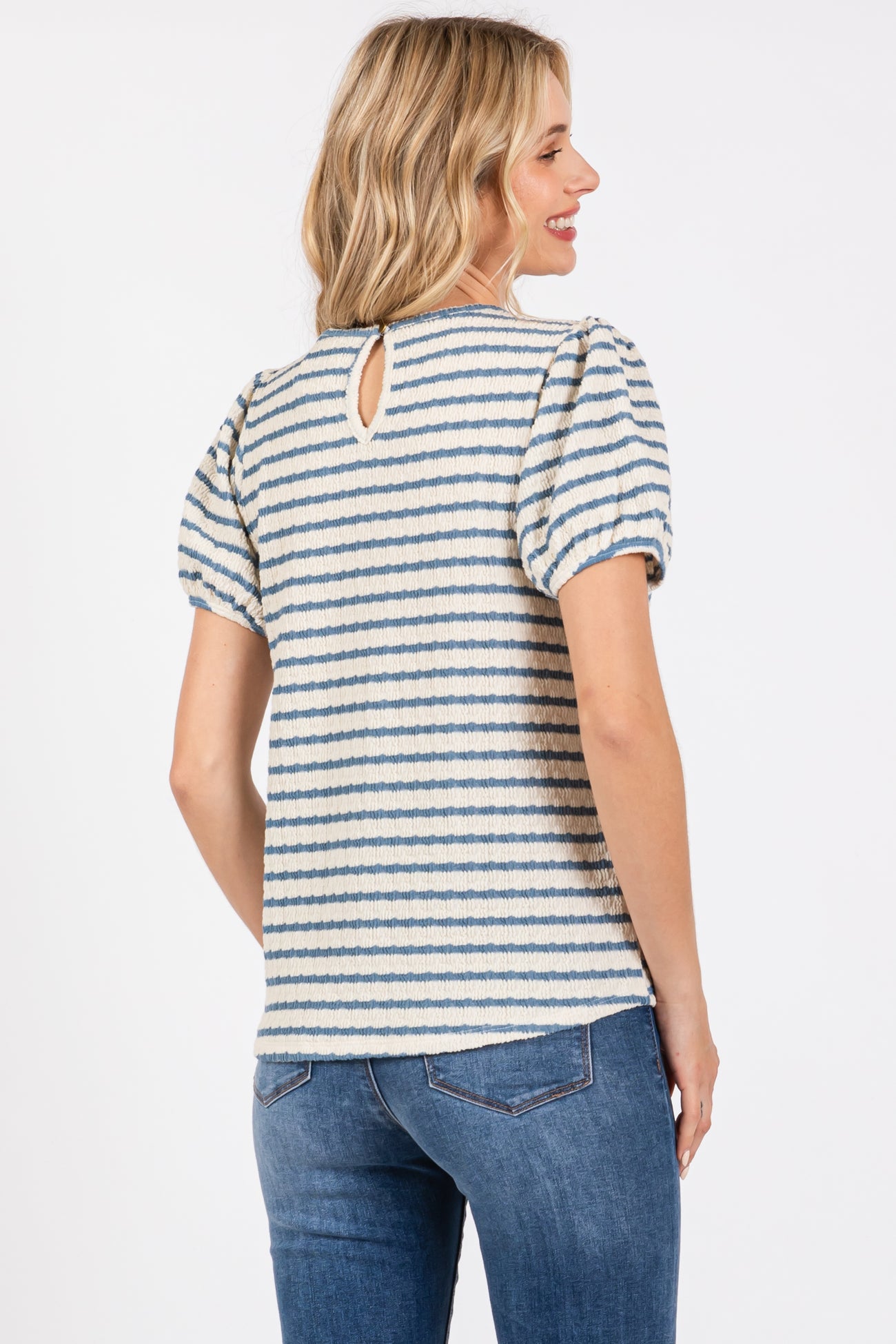 woman wearing a striped short sleeve top with puffed sleeves and a keyhole back, paired with jeans
