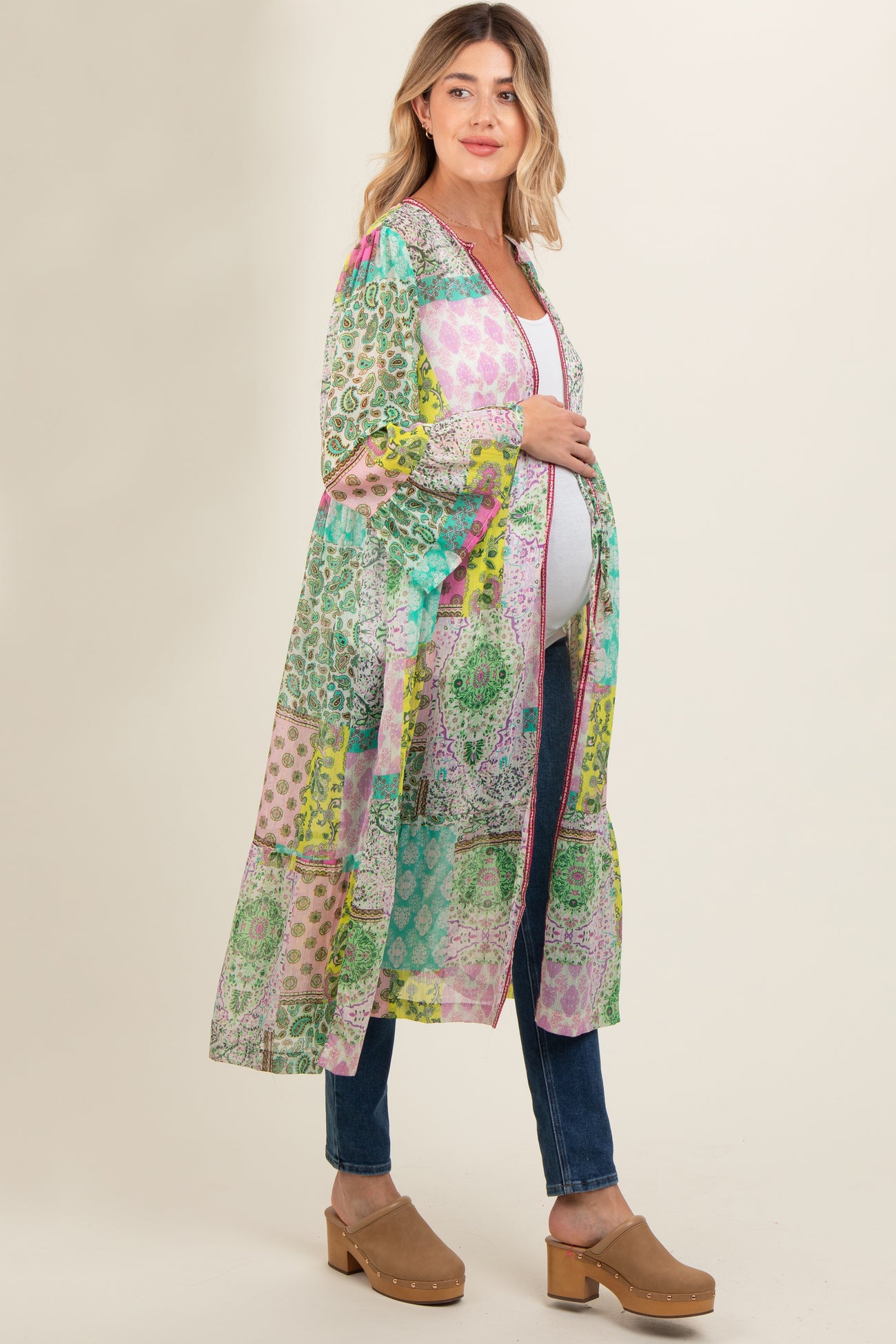 woman wearing a colorful patterned maternity kimono over a white top and blue jeans, showing her baby bump