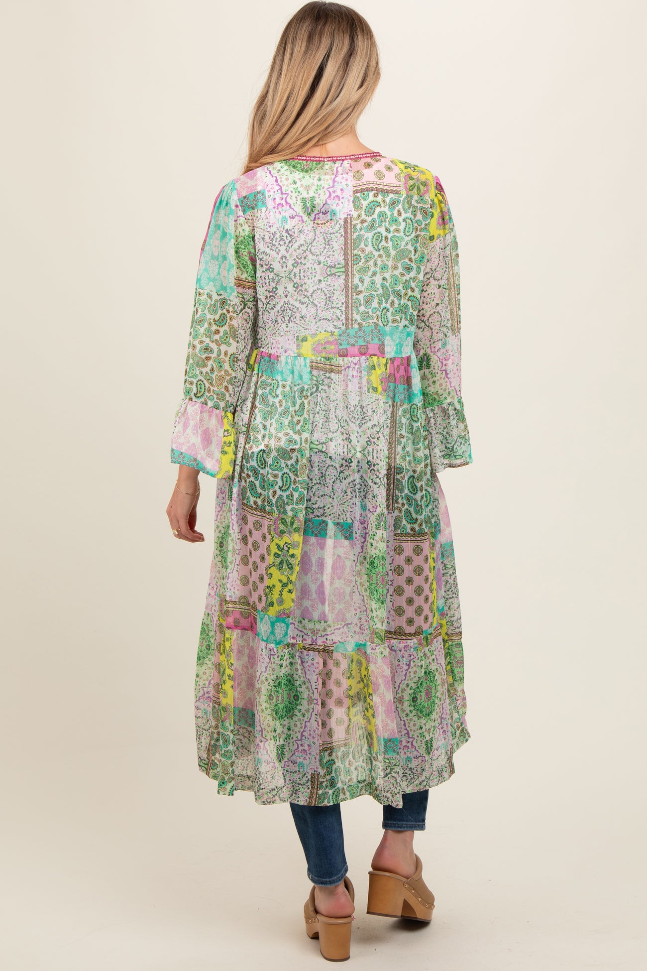 woman wearing a colorful patchwork long maternity dress with long sleeves and a tiered hem, seen from the back