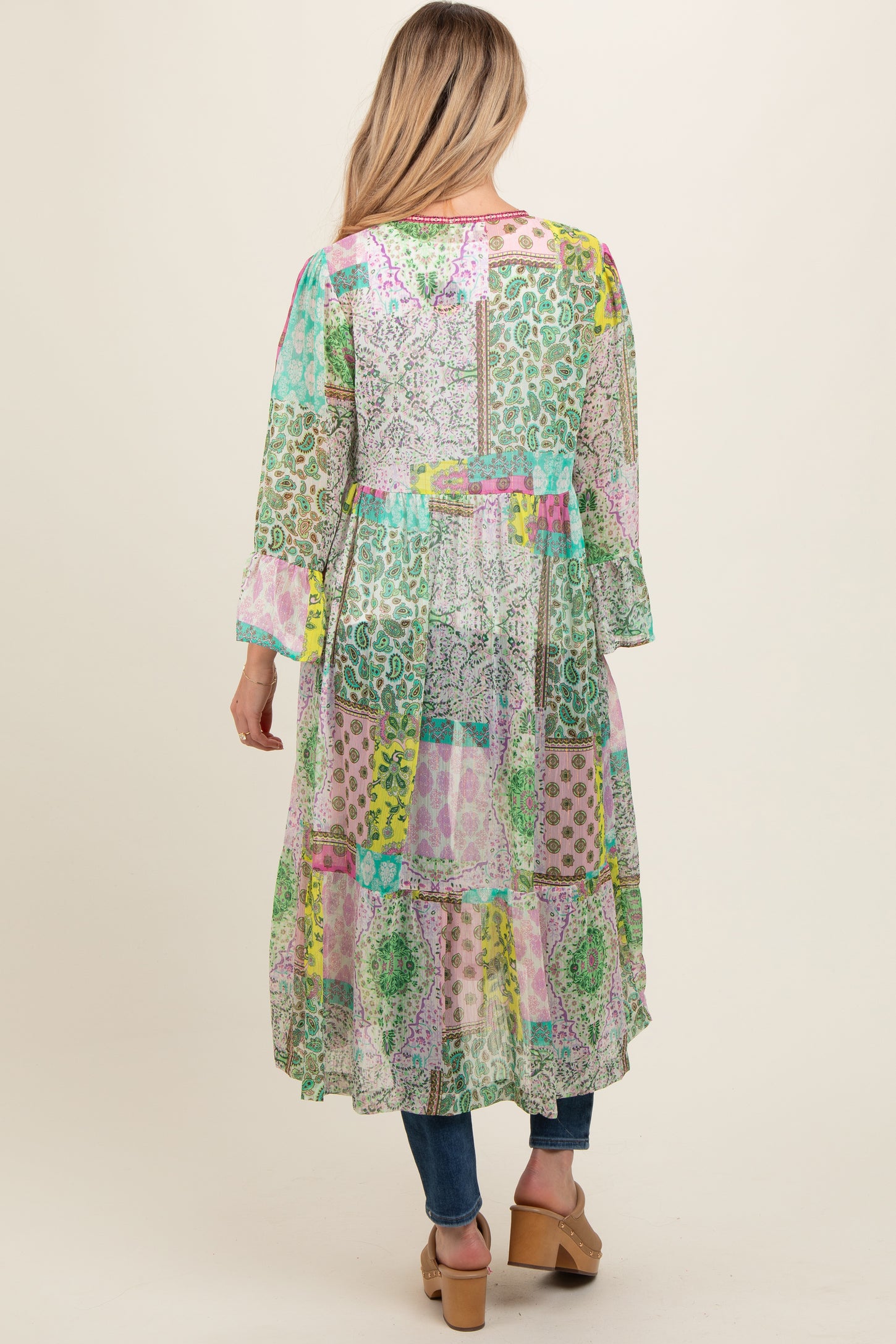 woman wearing a colorful patchwork long maternity dress with long sleeves and a tiered hem, seen from the back