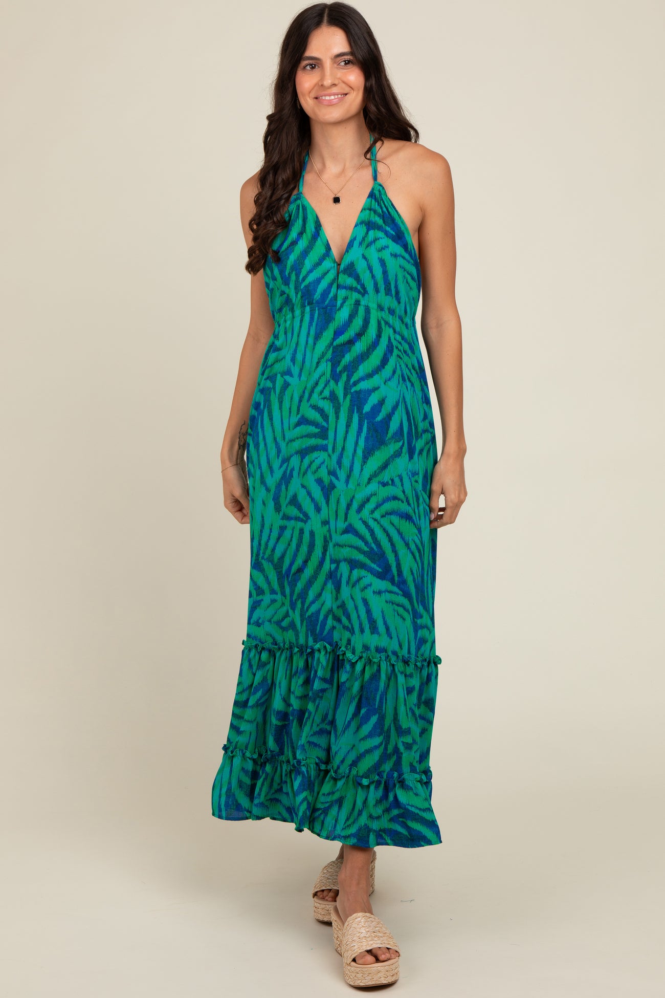 woman wearing a green and blue leaf print maxi dress with a halter neckline and ruffled hem