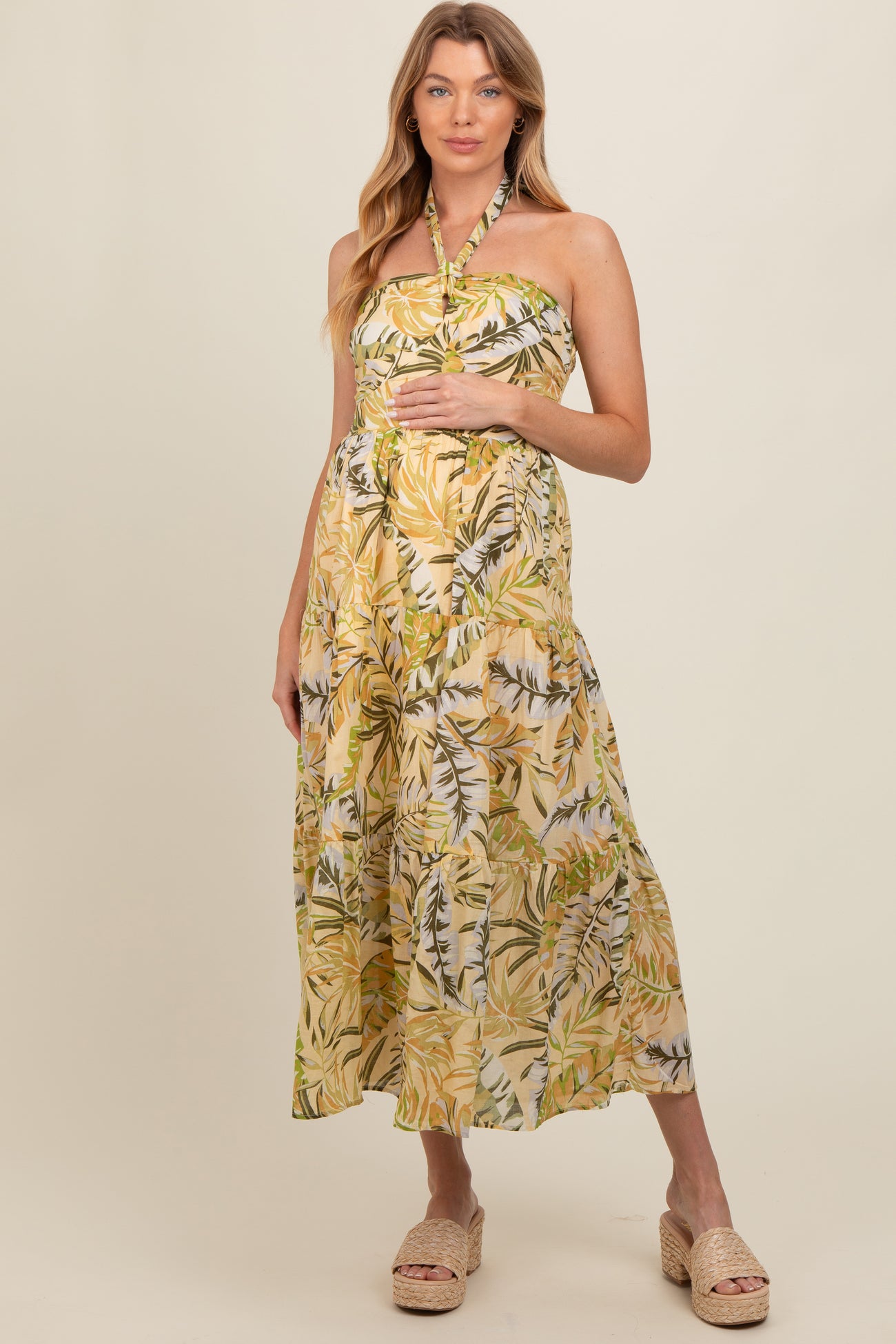 woman wearing a yellow tropical print maternity dress with a halter neck and a baby bump visible