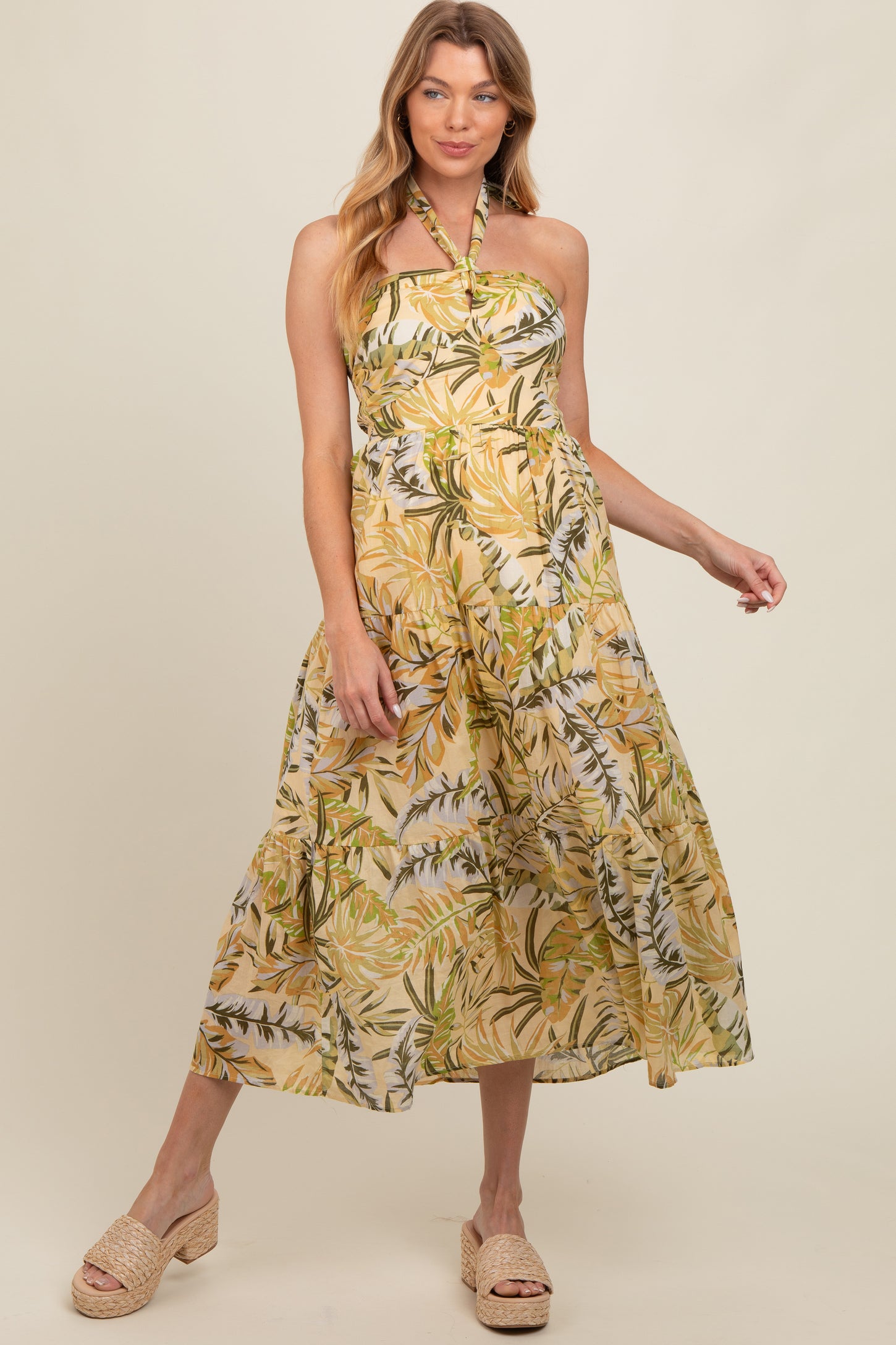 woman wearing a yellow floral maternity maxi dress with a halter neck and tiered skirt