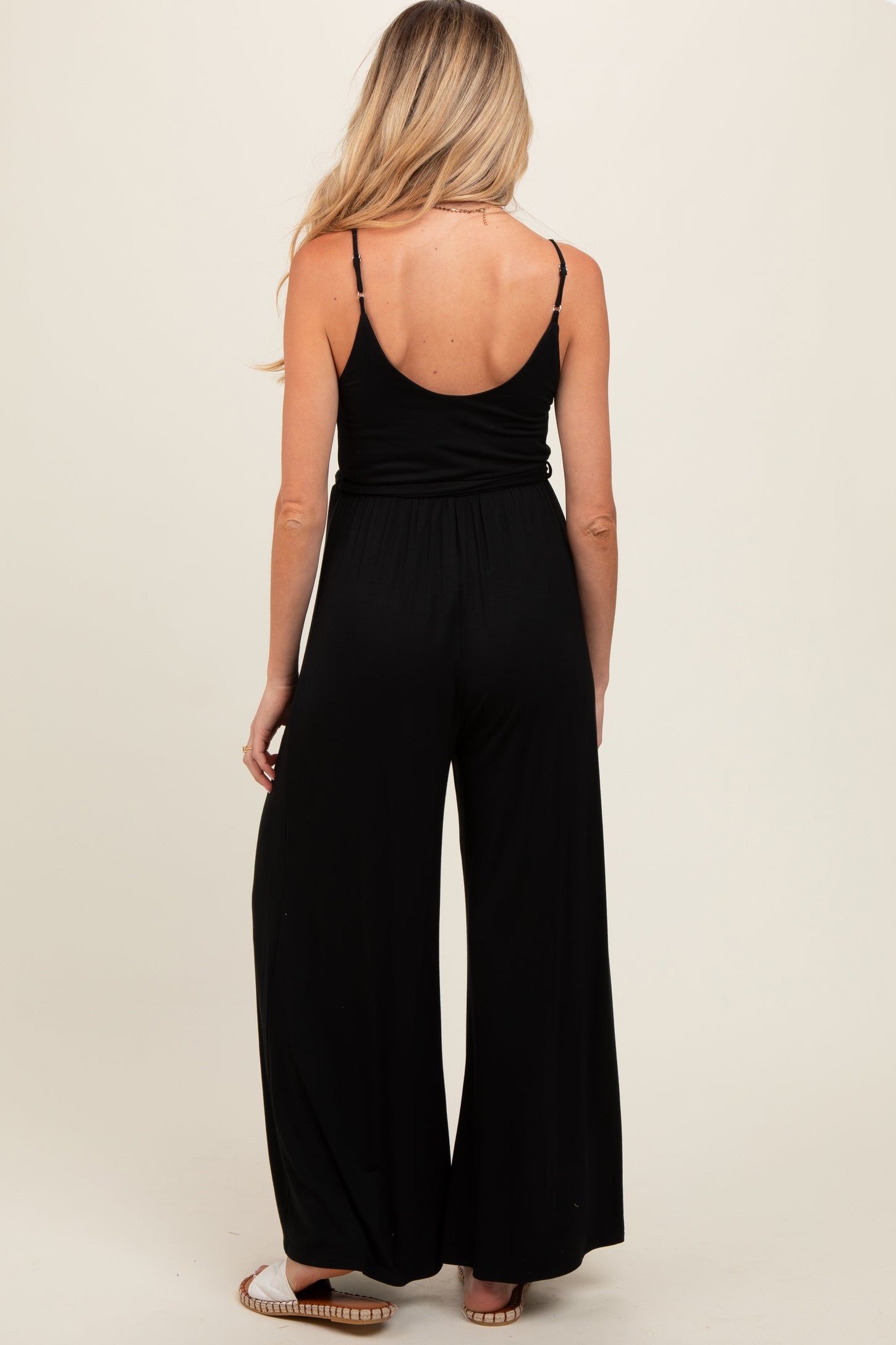 woman wearing a black maternity jumpsuit with a relaxed fit and spaghetti straps, viewed from the back