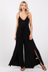 woman wearing a black sleeveless jumpsuit with a deep v-neck and side slits, tied at the waist