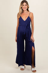 woman wearing a navy blue maternity jumpsuit with a plunging neckline, side slits, and a waist tie, showcasing her baby bump