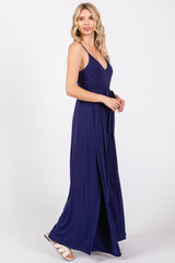 woman wearing a navy blue maxi dress with a deep v-neckline and a tie belt, standing in profile with a slit at the side