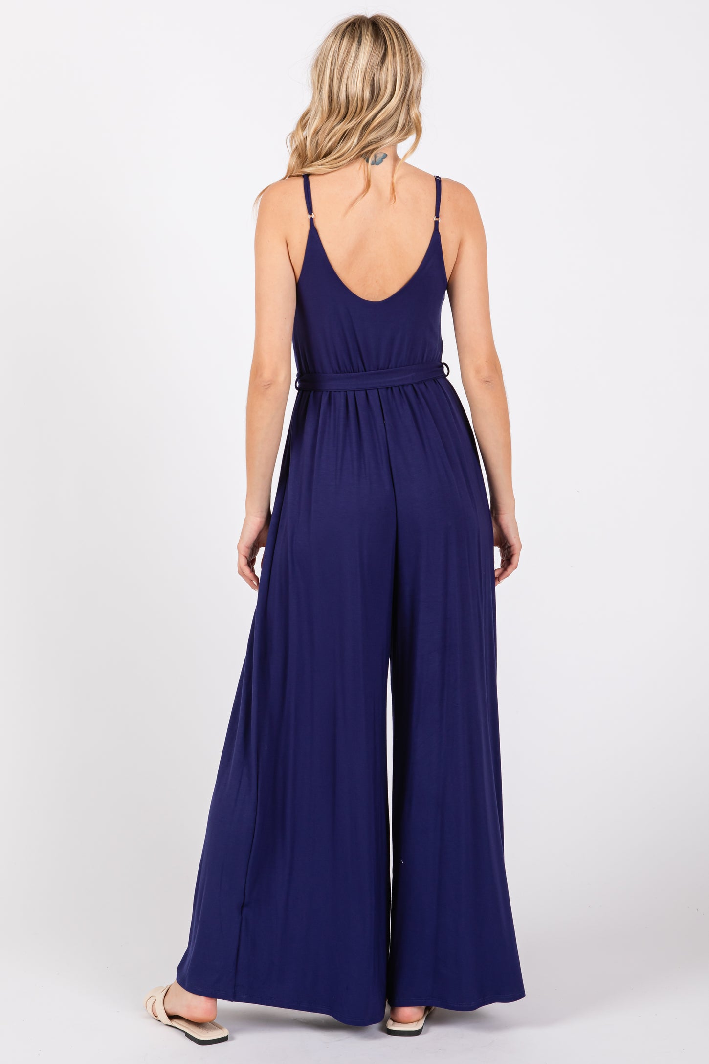 woman wearing a navy blue sleeveless jumpsuit with wide legs and a low back, standing with her back facing the camera