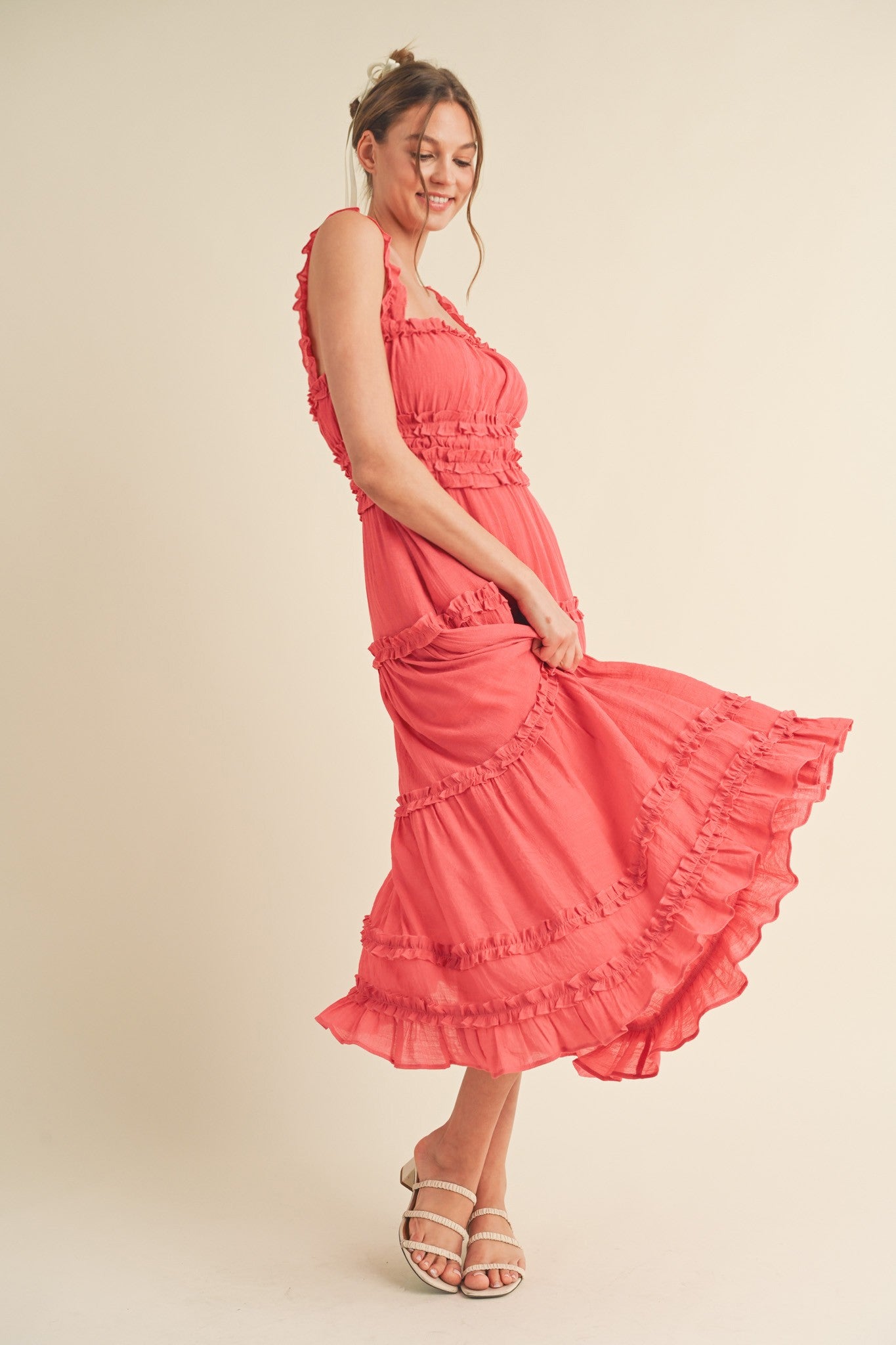 woman wearing a coral ruffled maxi dress with a fitted bodice and flared skirt, posing with a playful expression