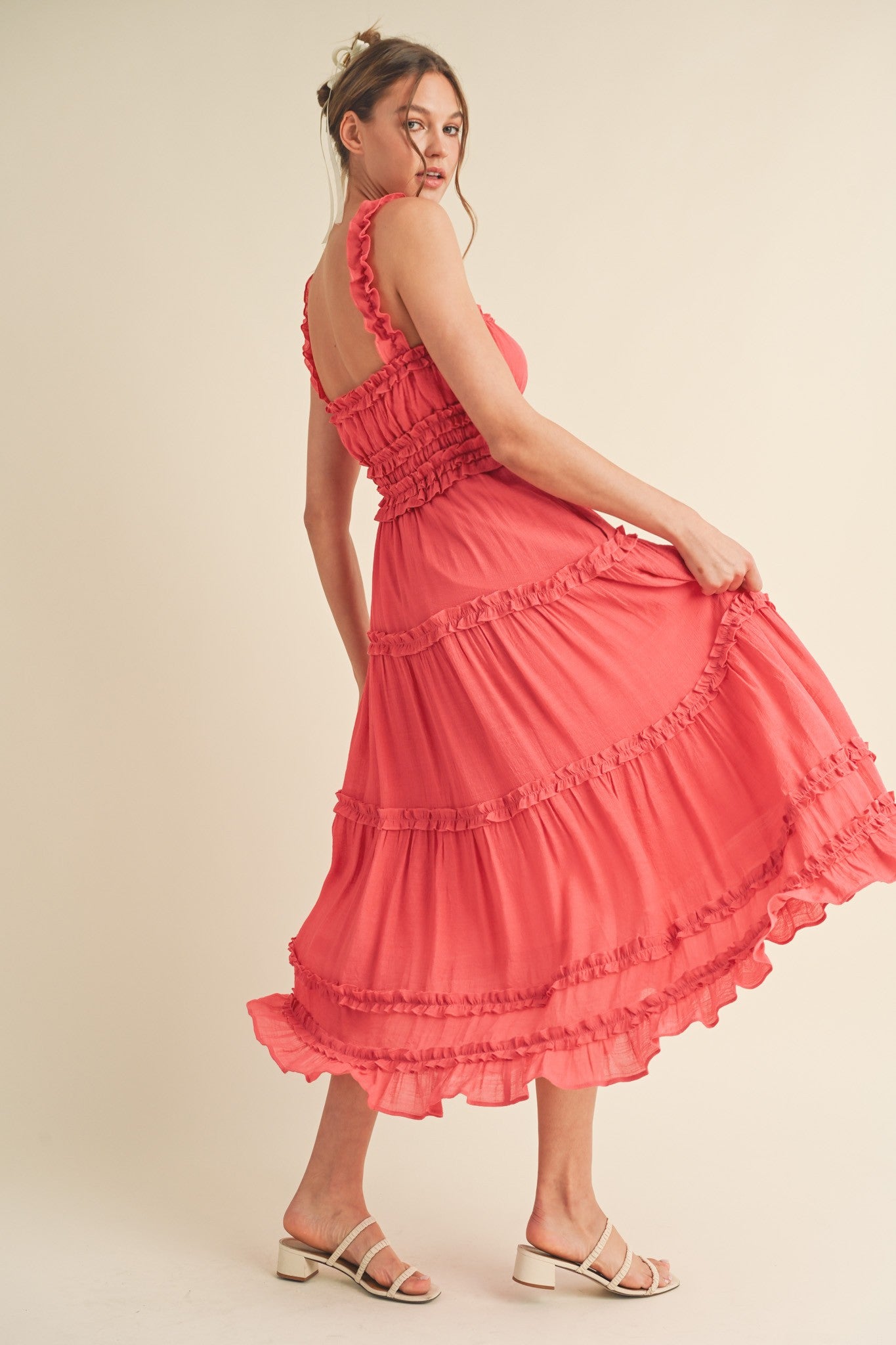woman wearing a coral midi dress with ruffle details and a smocked bodice, twirling in a light, airy style