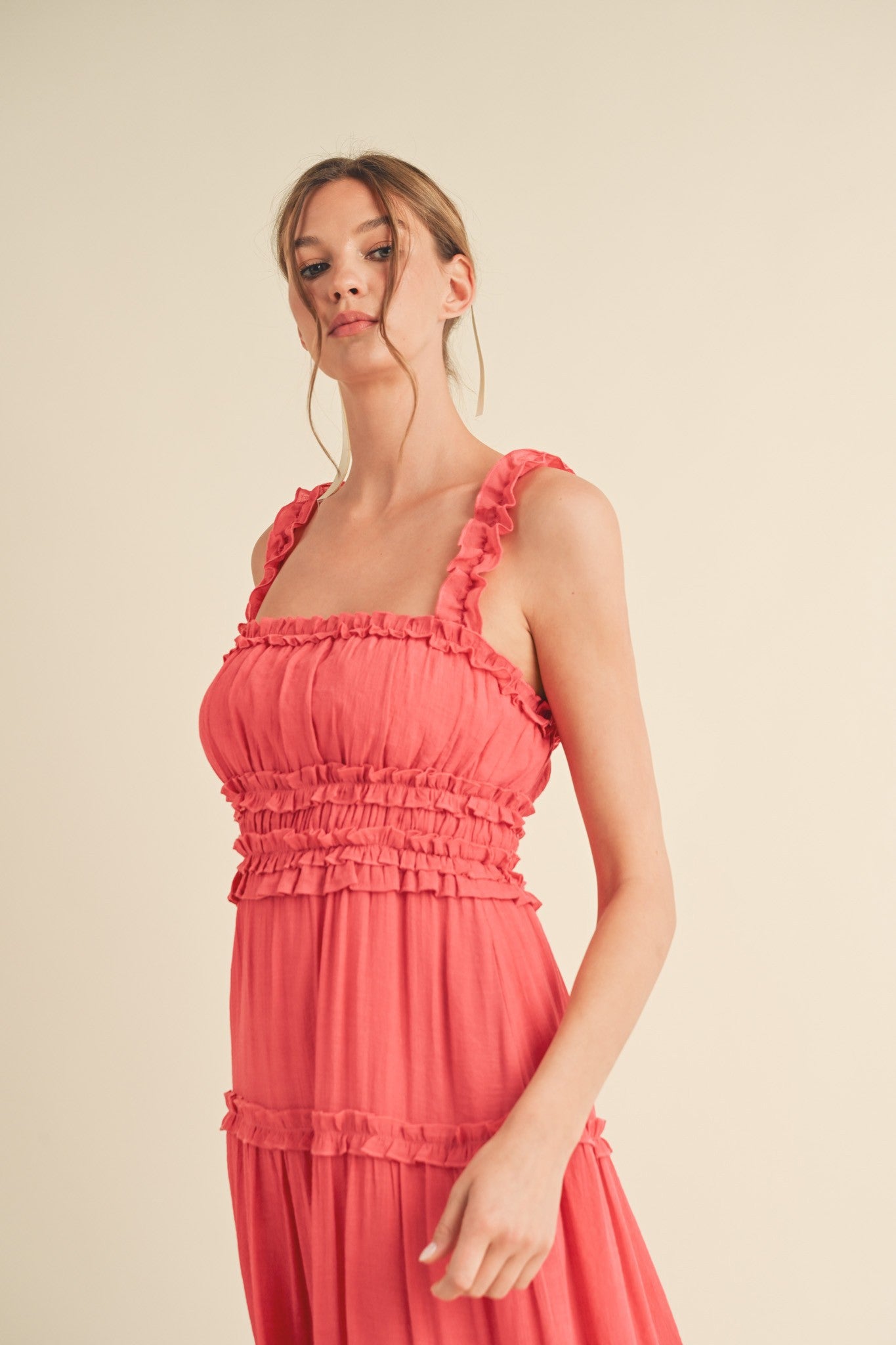 woman wearing a coral sleeveless maxi dress with ruffled straps and tiered detailing