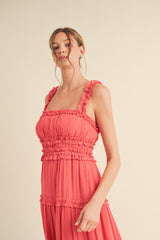 woman wearing a coral sleeveless maxi dress with ruffled straps and tiered detailing