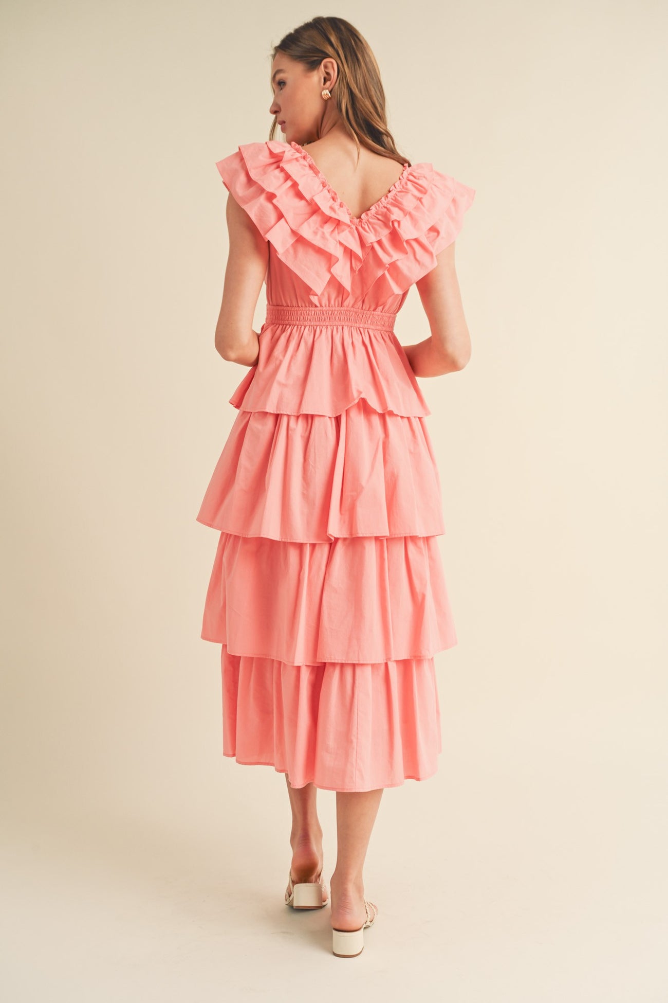 woman wearing a pink tiered maxi dress with ruffled sleeves and a smocked back, viewed from the back