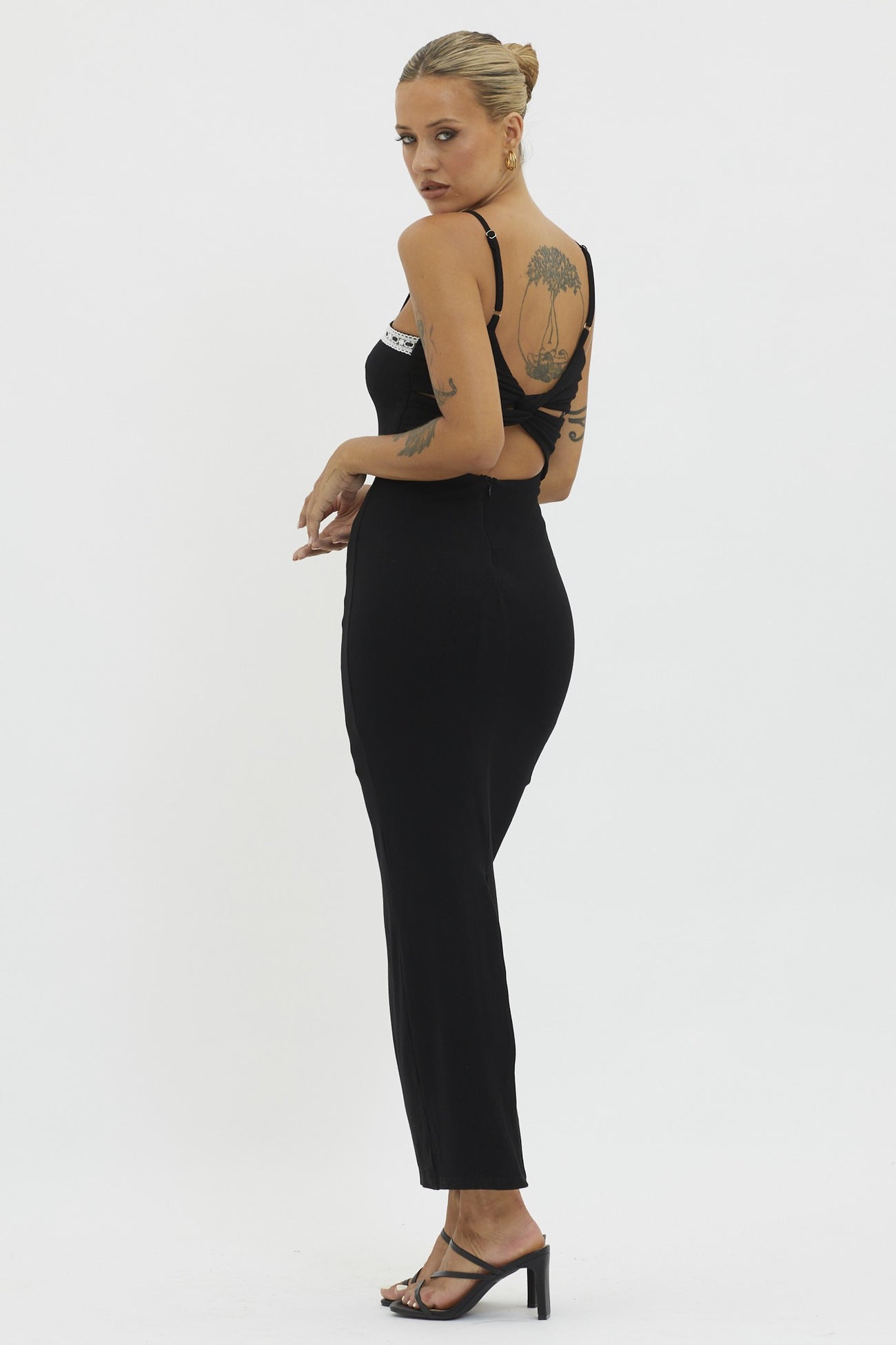 woman wearing a black fitted jumpsuit with a back cutout and spaghetti straps, standing in profile