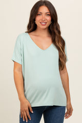 woman wearing a light green maternity top with a v-neck and short sleeves, showing her baby bump