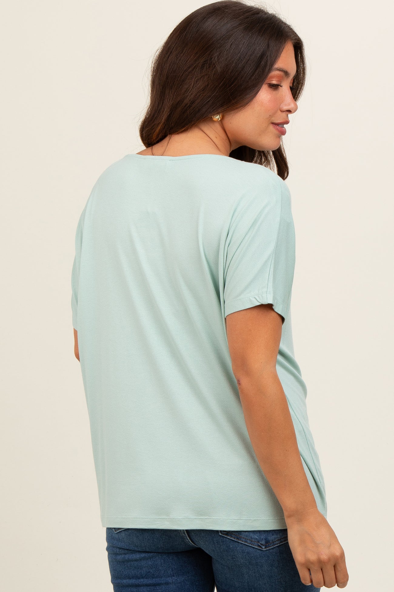 woman wearing a light green short sleeve maternity top, showing a relaxed fit and side view of her pregnant belly