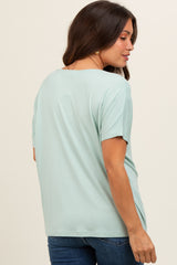 woman wearing a light green short sleeve maternity top, showing a relaxed fit and side view of her pregnant belly