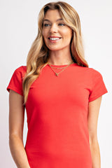 woman wearing a red short sleeve top and layered gold necklaces, smiling at the camera
