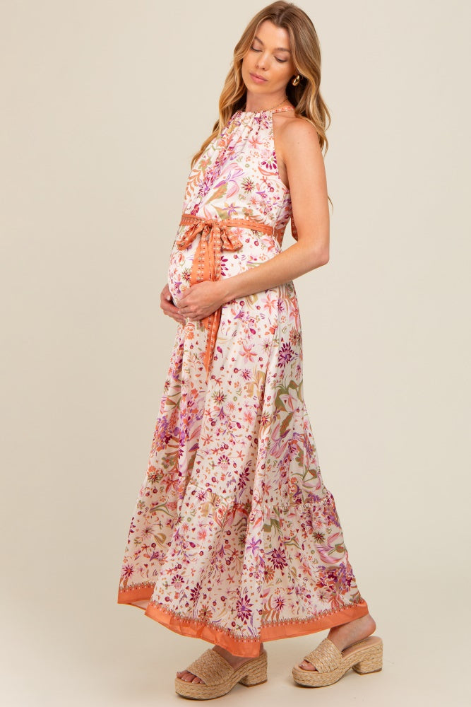 woman wearing a floral print maternity maxi dress with a halter neck and tied waist, showing her baby bump