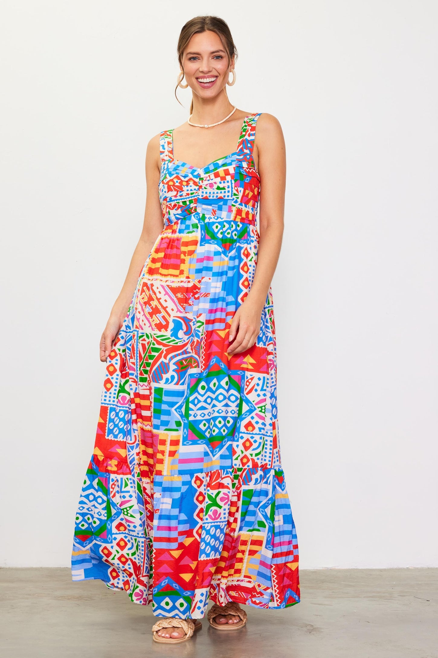 woman wearing a colorful patterned maxi dress with a fitted bodice and flowing skirt, smiling against a white background