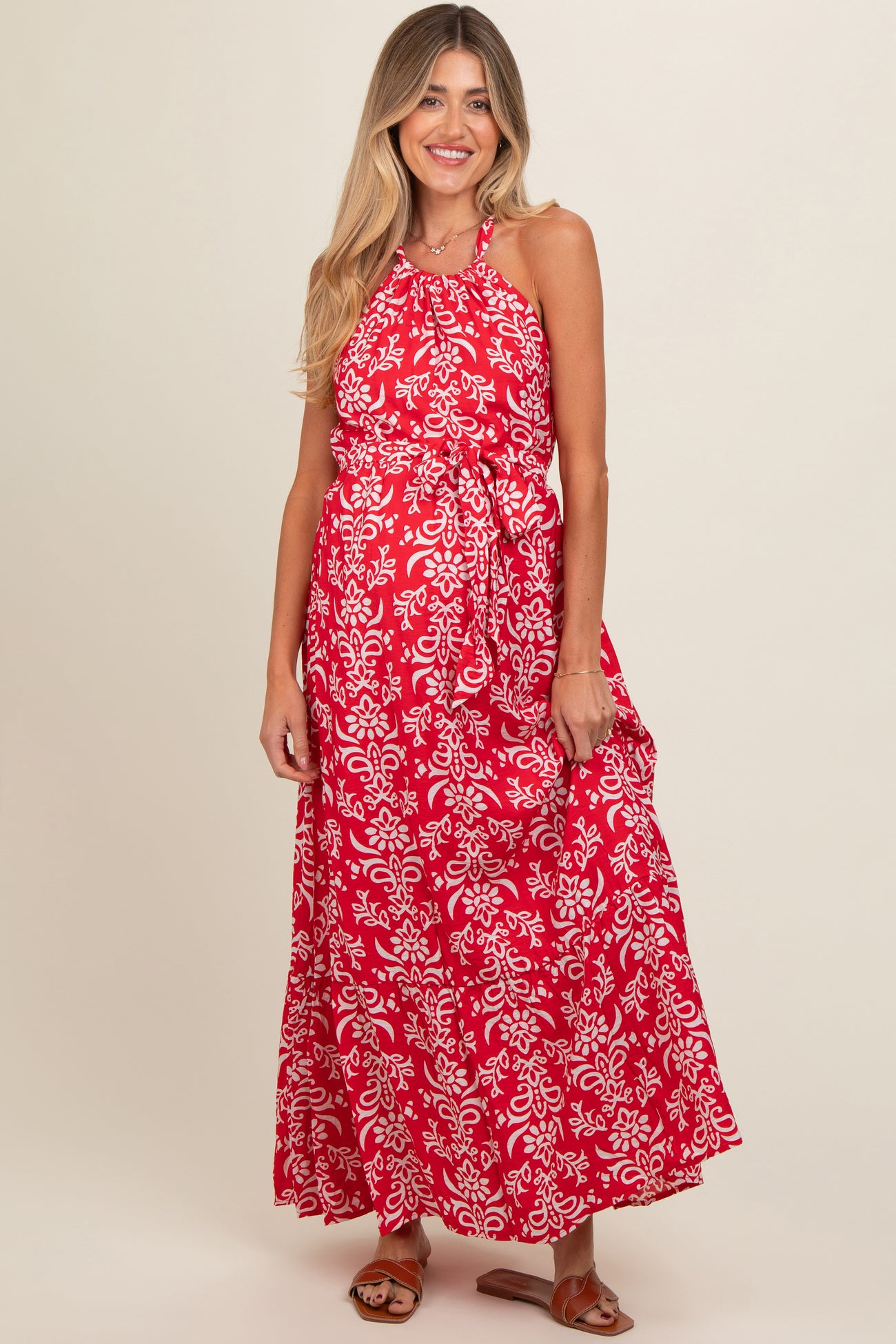 woman wearing a red floral print maternity maxi dress with a halter neckline and tie waist, showing a baby bump