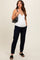 woman wearing a white maternity tank top and navy maternity pants, holding a black handbag, showing her baby bump