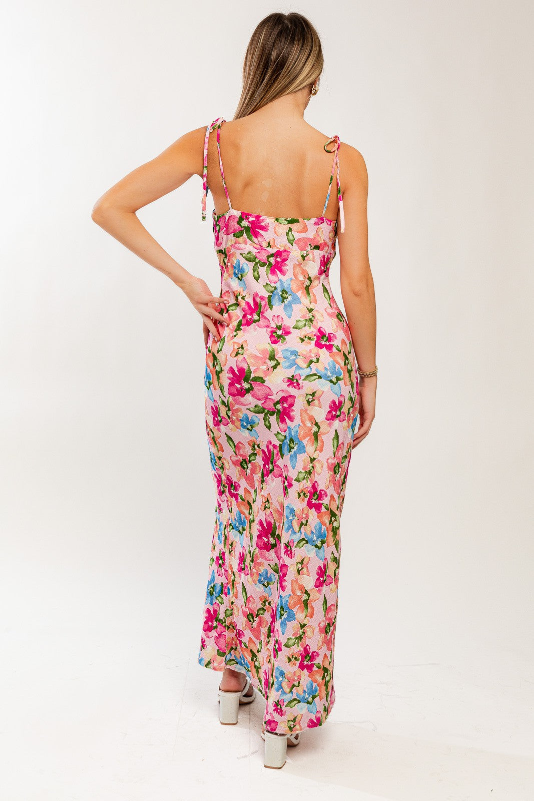 woman wearing a floral maxi dress with a pink background and tie shoulder straps, showing the back view