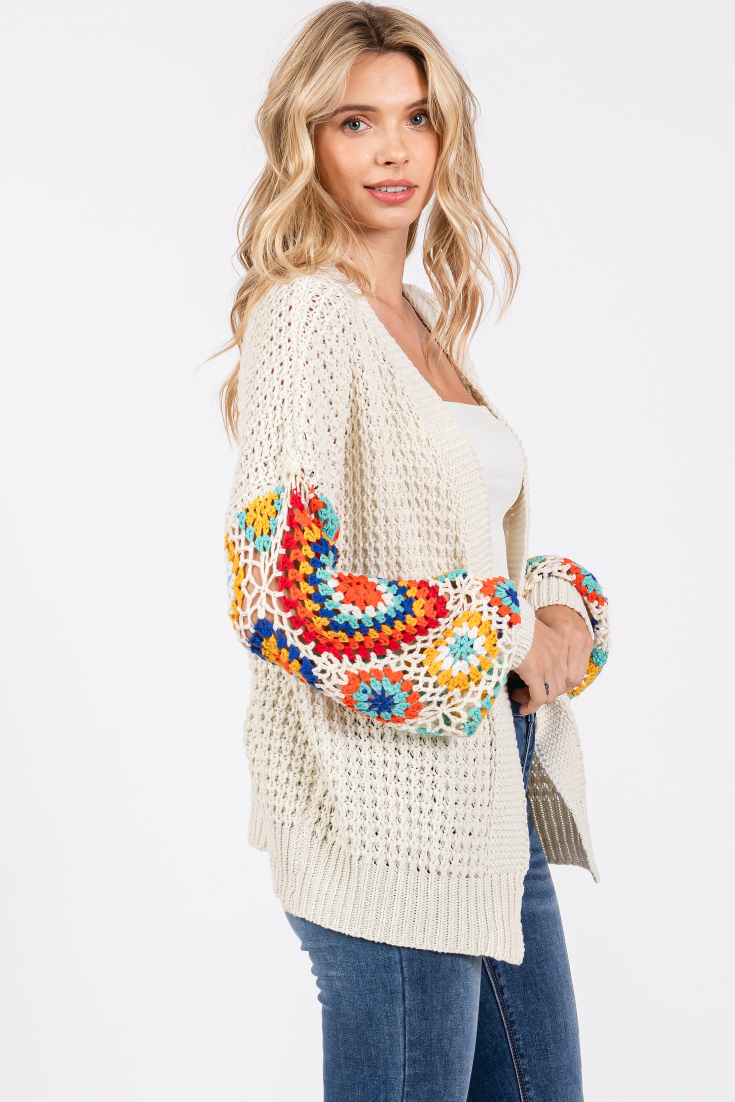 woman wearing a cream chunky knit cardigan with colorful crochet sleeves and paired with blue jeans