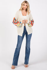 woman wearing a cream oversized cardigan with colorful crochet sleeves and flared jeans