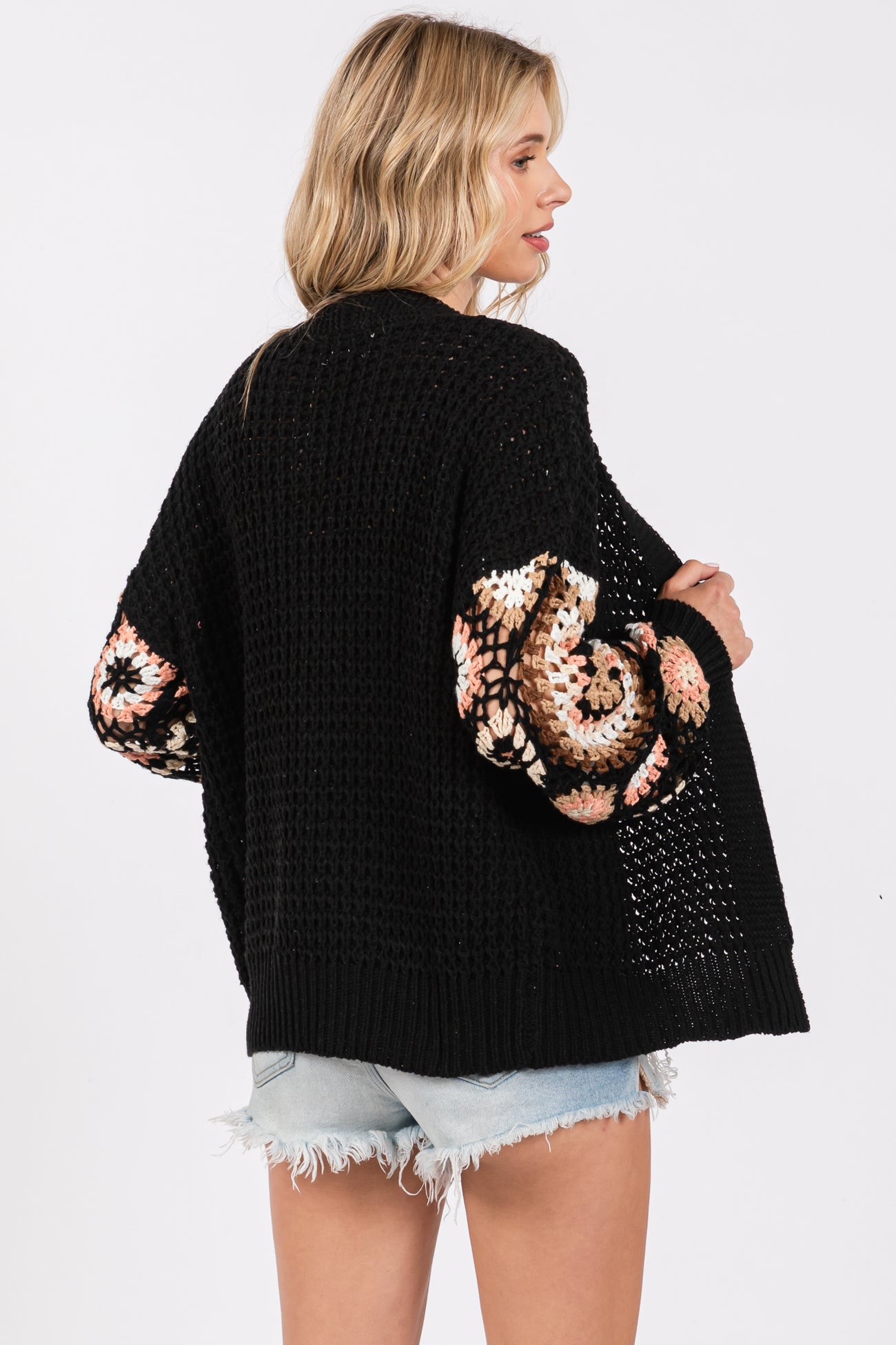 woman wearing a black knitted cardigan with colorful patterned sleeves and distressed denim shorts