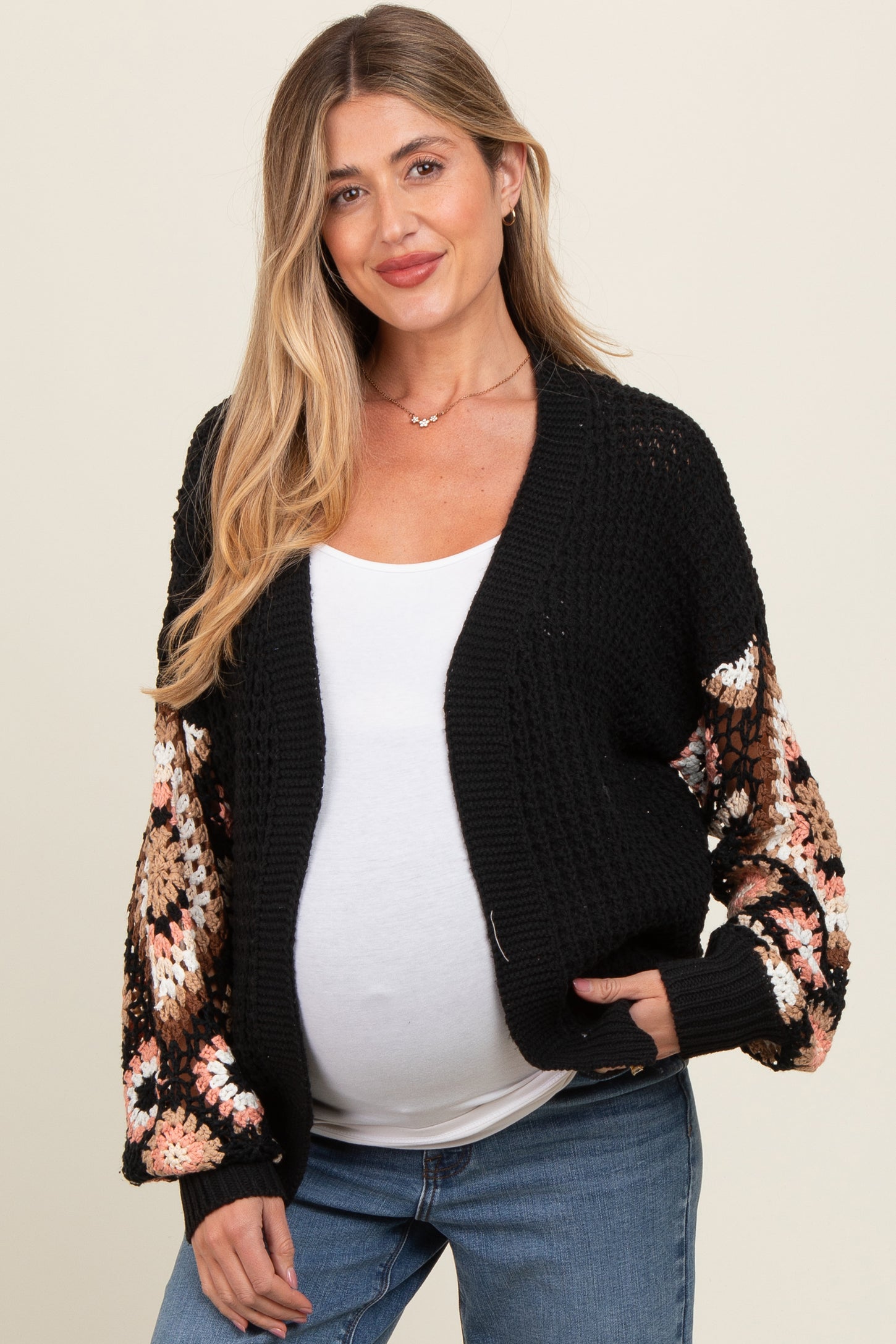 woman wearing a black maternity cardigan with colorful floral crochet sleeves and a visible baby bump