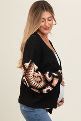 woman wearing a black maternity cardigan with colorful knit sleeves and holding her baby bump