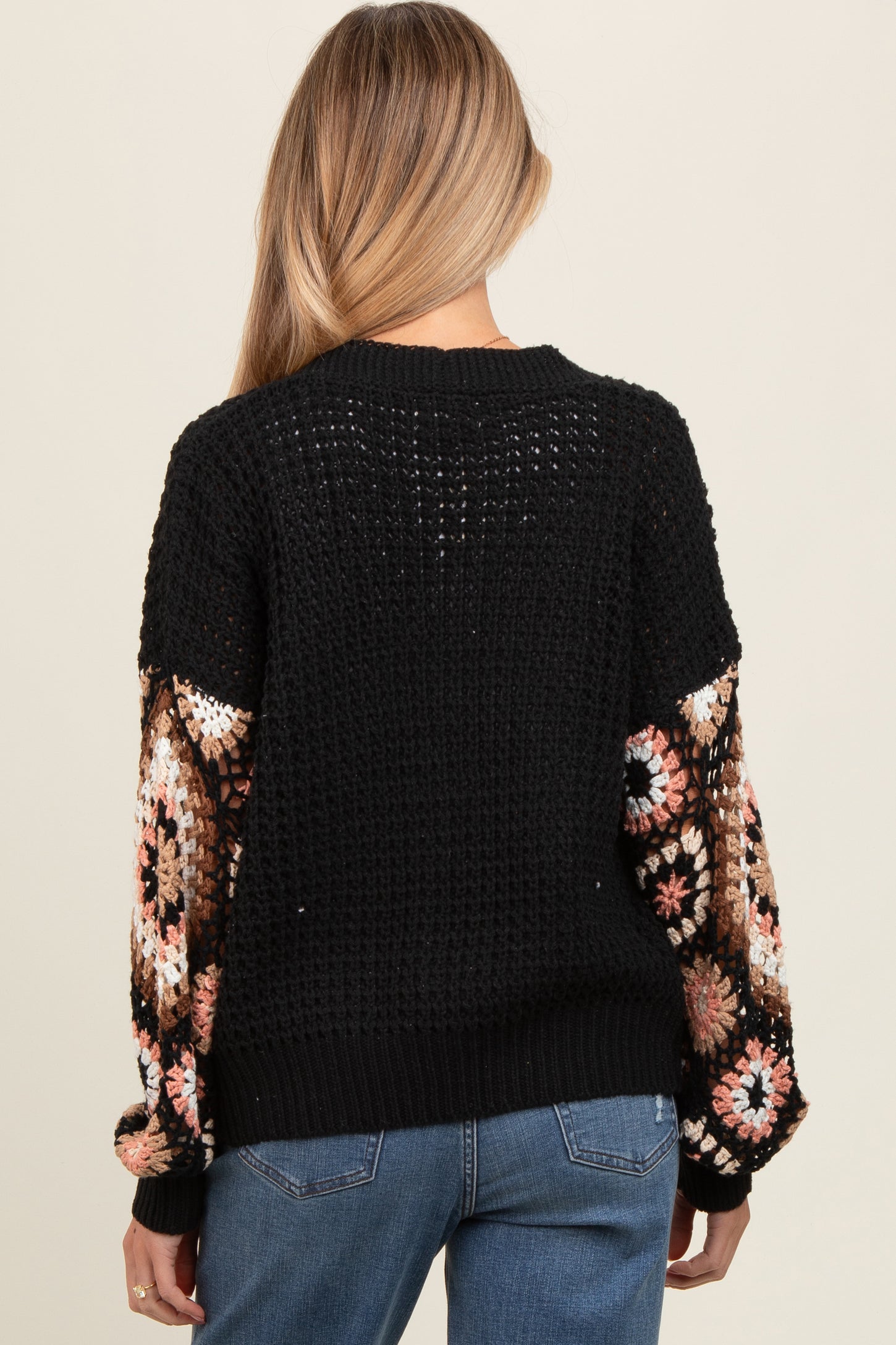 woman wearing a black crochet maternity sweater with patterned sleeves, viewed from the back