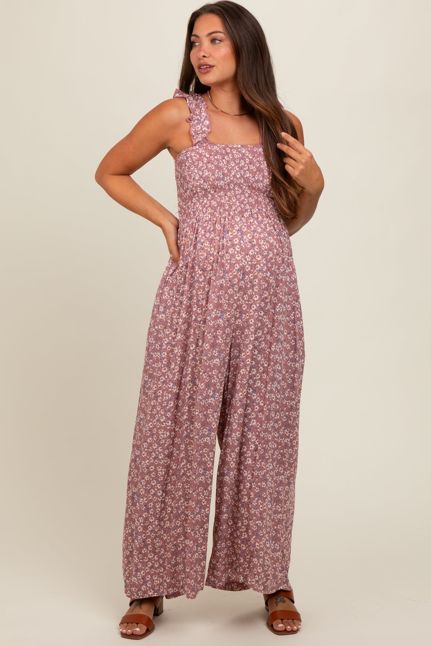 woman wearing a floral print maternity jumpsuit with a smocked bodice and ruffle strap details, showcasing her baby bump