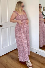 woman wearing a pink floral maternity dress with ruffle straps and a visible baby bump, standing in front of a mirror