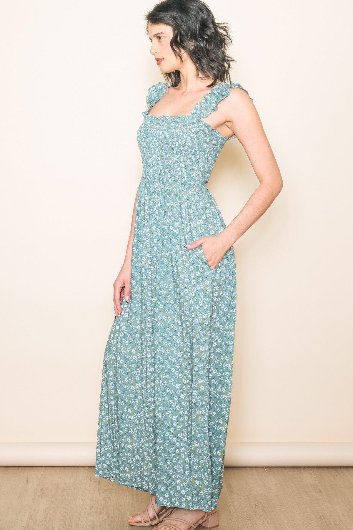 woman wearing a teal floral maxi dress with ruffled straps and pockets, standing sideways against a neutral background