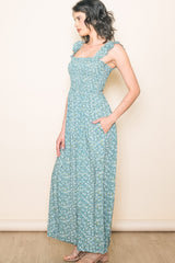 woman wearing a teal floral maxi dress with ruffled straps and pockets, standing sideways against a neutral background