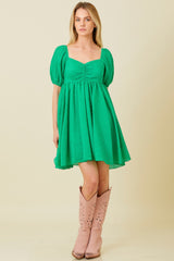 woman wearing a green puff sleeve fit and flare dress with a square neckline and western-style boots