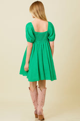 woman wearing a green smocked mini dress with puff sleeves and styled with pink knee-high boots